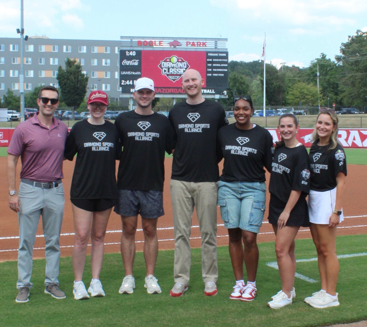 Seven members of the Diamond Sports Alliance team standing on the field at Bogle Park beneath the Diamond Classic scoreboard